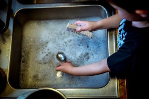 Child learns responsibility by helping to wash dishes.