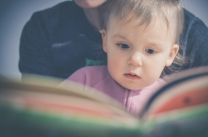 A small child reads a book with her mother.