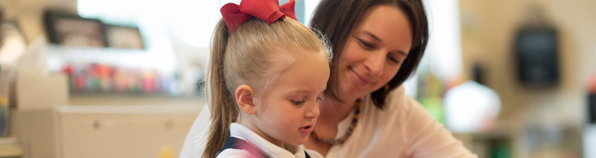 A teacher at Dayspring Christian Academy works with her PreK student at a desk in the classroom.