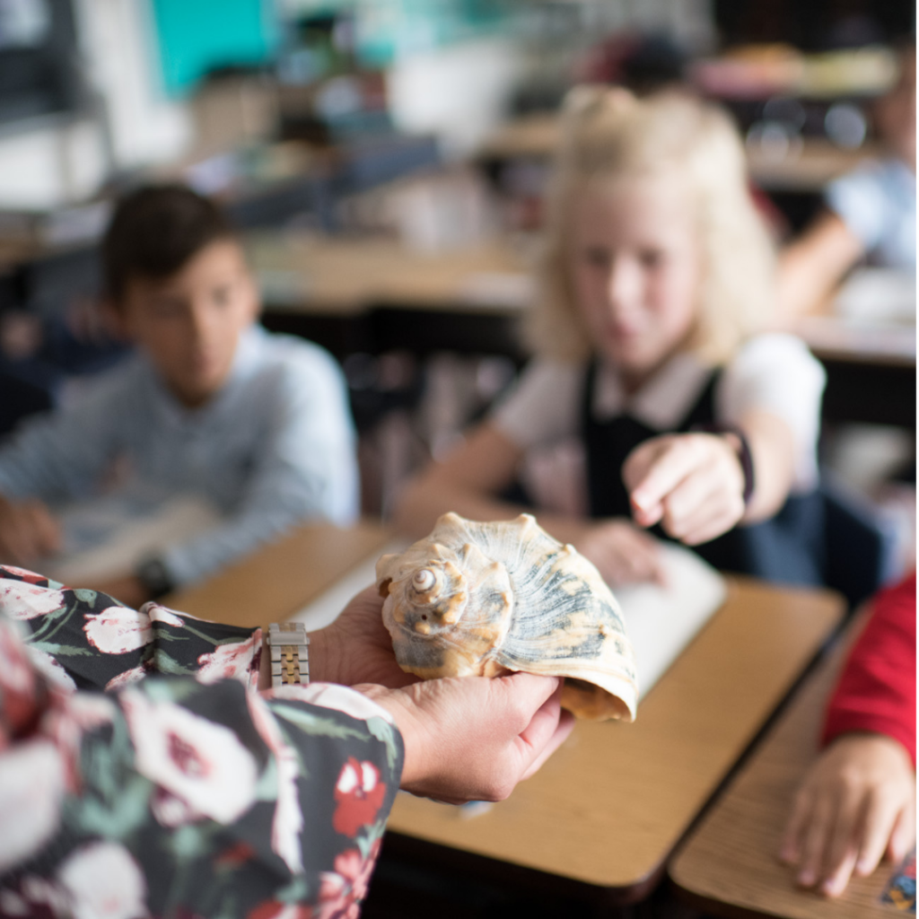 A teacher holding a sea shell out to a student at Dayspring Christian Academy